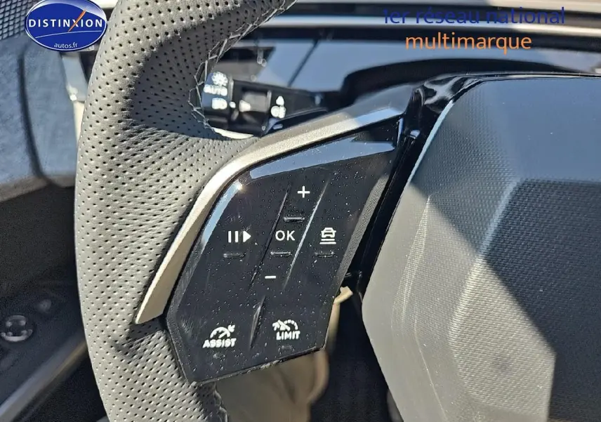 Gros plan sur les commandes du volant cuir perforé du Peugeot 5008 Hybrid 145 GT gris titane 2025.