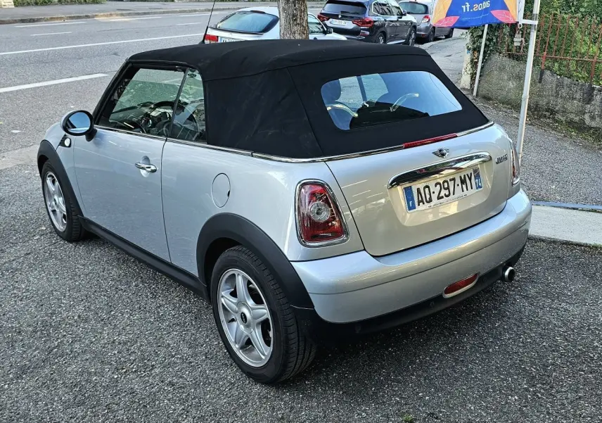 Vue 3/4 arrière droite d'une MINI Cabriolet R57 grise avec capote noire, jantes alliage et échappement chromé visible.