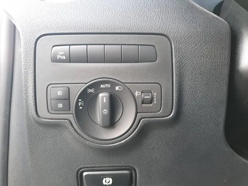 Gros plan sur le bouton de commande des phares et l'interrupteur du frein à main électrique du Mercedes Vito Fourgon blanc.