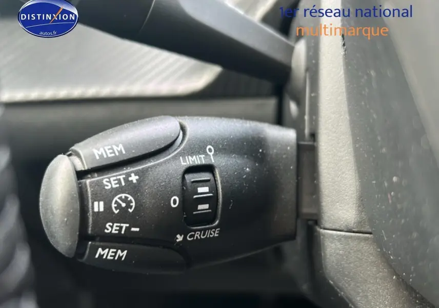 Gros plan sur la commande de régulateur de vitesse noire à gauche du volant dans une Peugeot 208 gris artense.