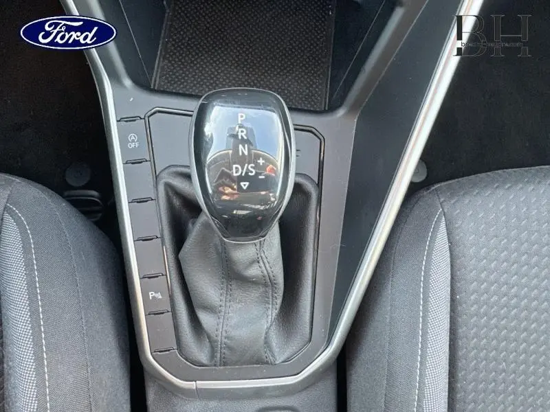 Levier de vitesses automatique noir en gros plan entre les sièges tissu gris d'une Volkswagen Taigo blanche.