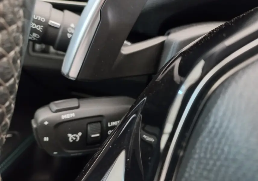 Gros plan sur la commande de régulateur de vitesse à gauche du volant du Peugeot 5008 gris foncé, intérieur noir.