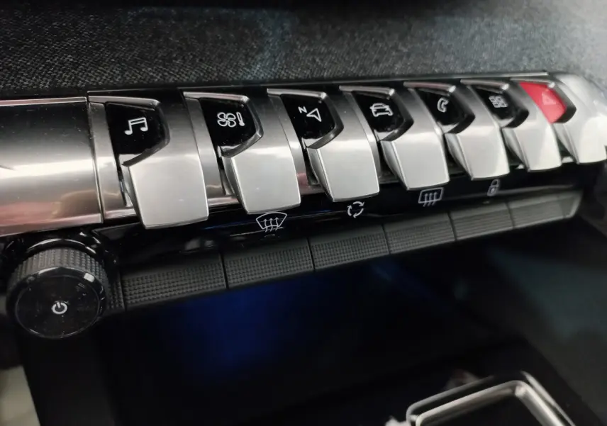 Gros plan sur les commandes chromées du tableau de bord du Peugeot 5008 gris foncé, avec boutons multifonctions et climatisation.