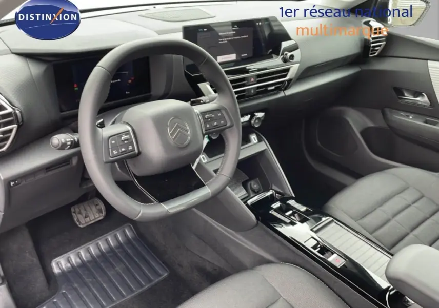 Vue intérieure côté conducteur de la Citroën C4 2026 blanche métal, avec tableau de bord noir et volant multifonction.
