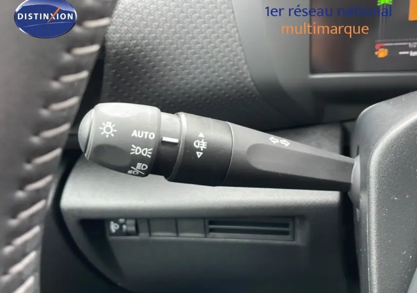 Gros plan sur la commande des phares et clignotants à gauche du volant dans l’habitacle noir d’une Citroën C4 blanche.