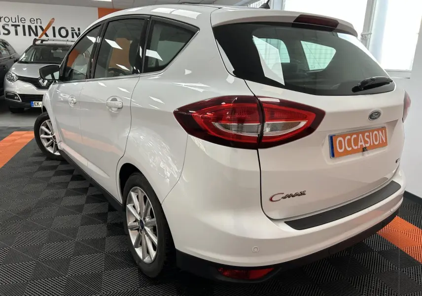 Vue 3/4 arrière droite d'une Ford C-MAX blanche 2018 en showroom avec plaque "OCCASION" visible.