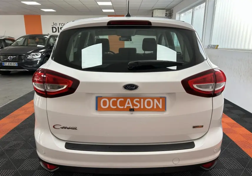 Vue arrière d'un Ford C-MAX blanc 2018 avec logo, feux rouges et plaque "OCCASION" en intérieur showroom.
