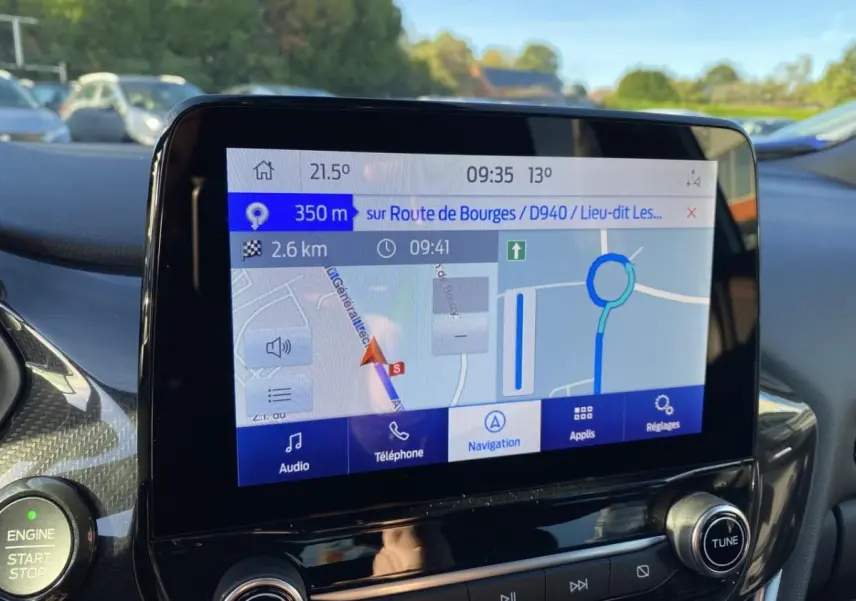Écran GPS couleur du tableau de bord du Ford Puma gris, avec commandes audio et bouton start/stop visibles.