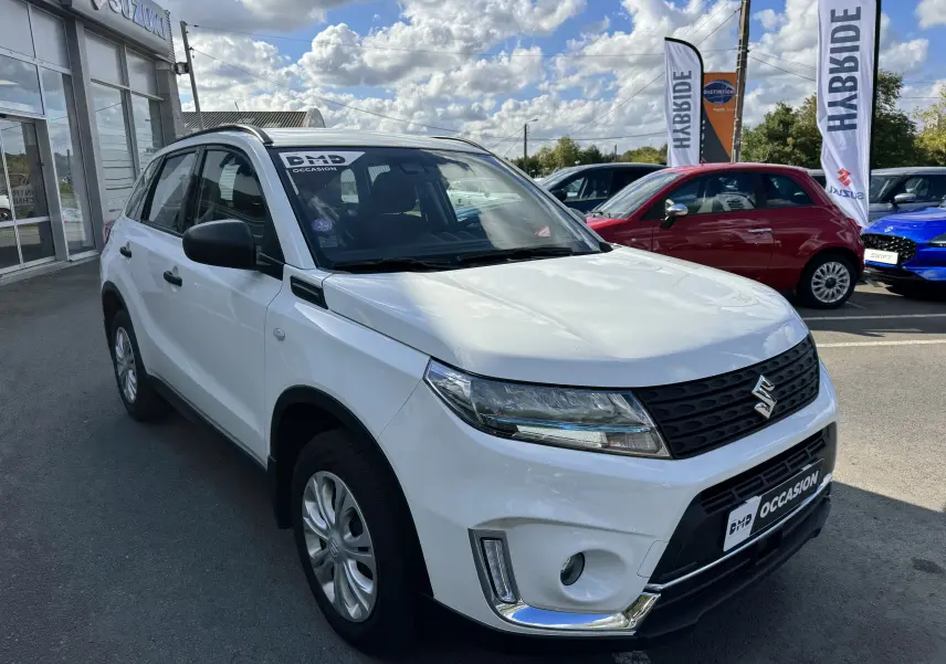 Suzuki Vitara blanc vue 3/4 avant droit, SUV hybride 2023 avec calandre noire et jantes argentées.