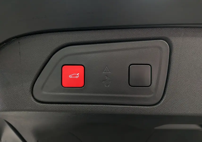 Gros plan sur le bouton rouge d'ouverture électrique du coffre dans l'habitacle noir du Citroën C5 Aircross hybride 2025.