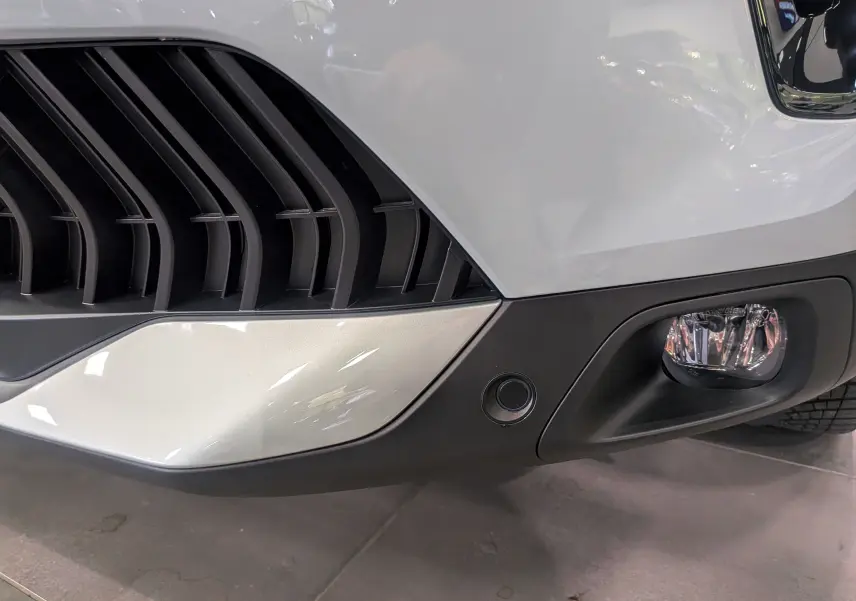 Gros plan sur le pare-chocs avant droit blanc Okénite du Citroën C5 Aircross hybride avec antibrouillard et capteur de stationnement.