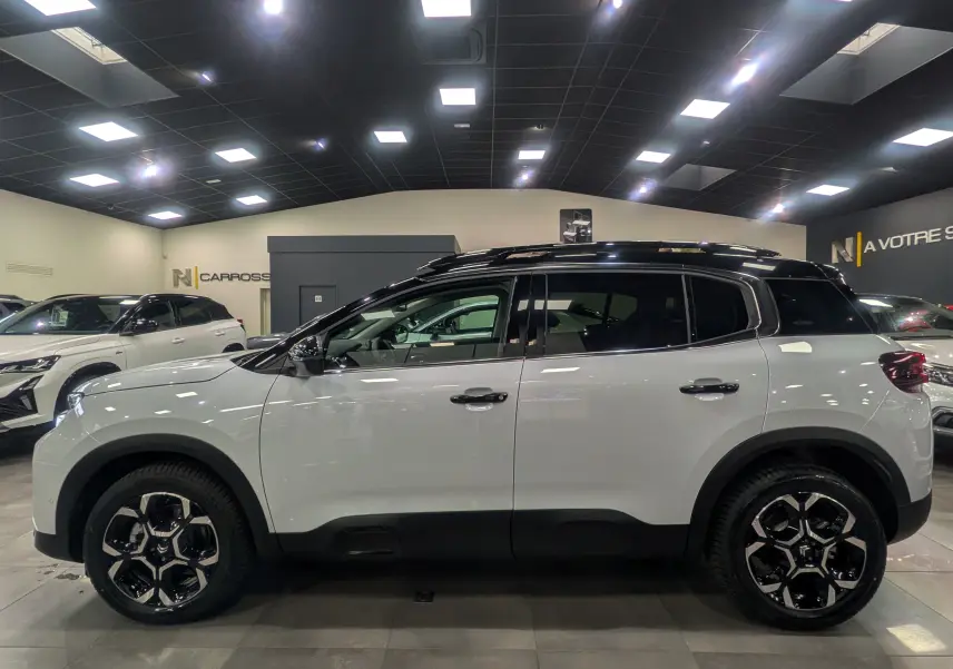 Vue de profil côté gauche d'un Citroën C5 Aircross hybride blanc Okénite avec toit noir en showroom.