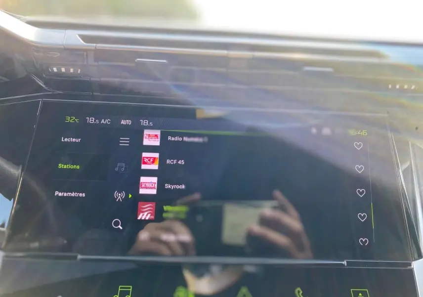 Écran tactile central de la Peugeot 308 Gris Selenium 2025 affichant les stations radio avec reflets du conducteur.