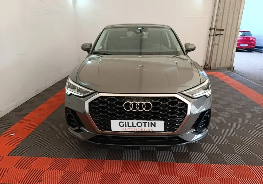 Vue avant d'un Audi Q3 Sportback 2024 gris métallisé avec calandre hexagonale et phares LED allumés.