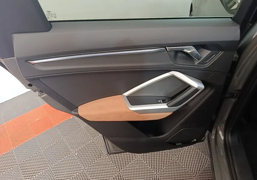 Vue rapprochée de la porte arrière droite de l'Audi Q3 Sportback 2024 avec garniture noire et accoudoir beige.