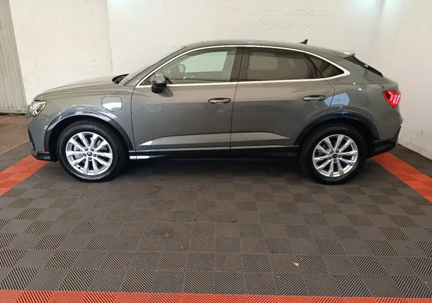 Vue de profil côté gauche d'un Audi Q3 Sportback hybride rechargeable gris métallisé avec jantes alliage et feux arrière allumés.