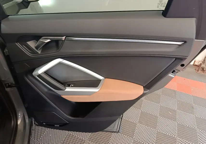 Vue intérieure côté gauche de la porte arrière d’un Audi Q3 Sportback 2024 avec garniture noire et insert marron clair.