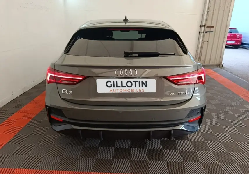 Vue arrière d'un Audi Q3 Sportback hybride rechargeable gris, avec feux LED allumés et logo distinctif sur coffre.
