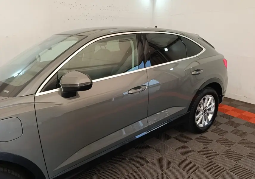 Vue latérale droite d'un Audi Q3 Sportback hybride rechargeable gris métallisé avec jantes argentées dans un garage.
