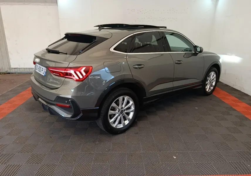 Audi Q3 Sportback gris vue 3/4 arrière droit, avec feux arrière LED allumés dans un garage.