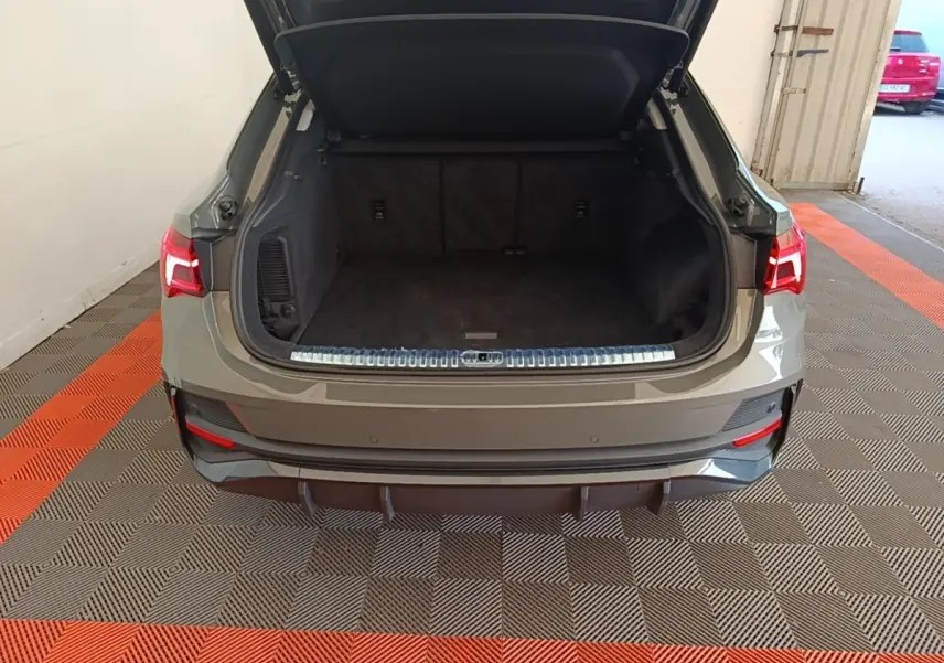Vue arrière de l'Audi Q3 Sportback 2024 gris, coffre ouvert montrant l'espace de chargement vide et les feux arrière allumés.