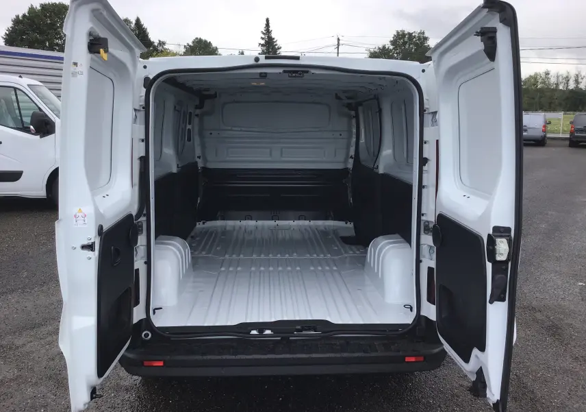 Vue arrière du Renault Trafic Fourgon blanc 2023 avec portes ouvertes montrant l'espace de chargement vide et spacieux.