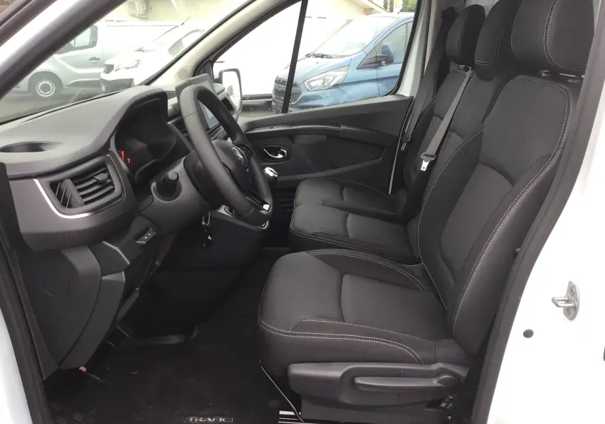 Intérieur du Renault Trafic Fourgon blanc 2023, vue côté conducteur montrant les sièges noirs et le tableau de bord.