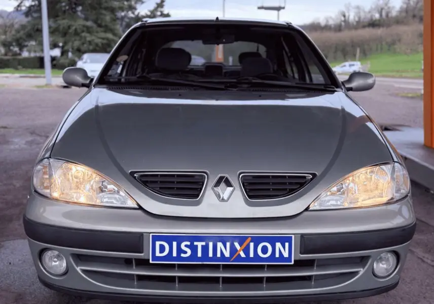 Vue frontale d'une Renault Mégane grise avec phares allumés et plaque d'immatriculation Distinxion visible.