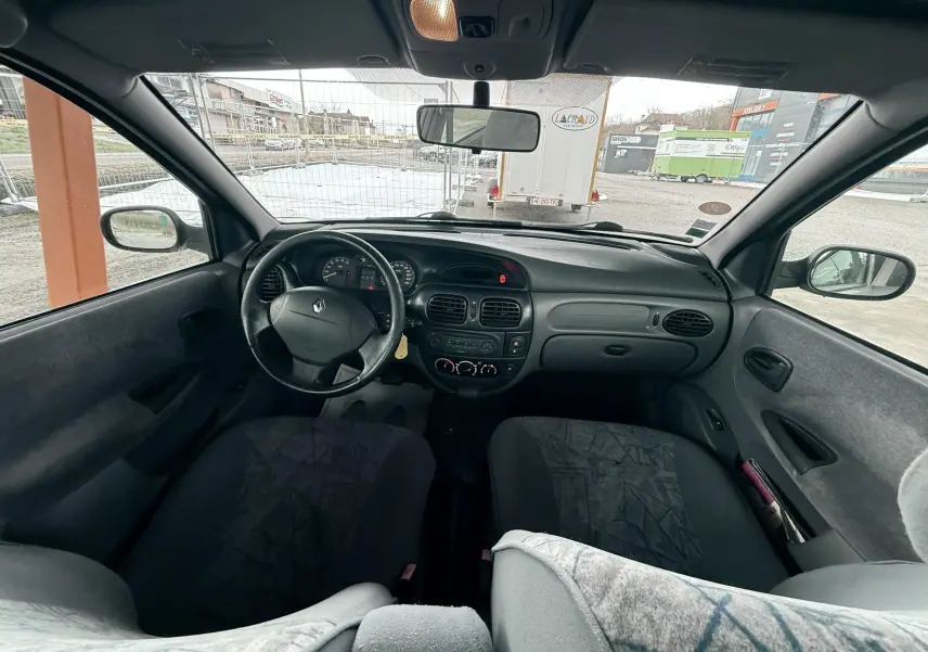 Vue intérieure avant de la Renault Mégane 2000, tableau de bord et volant noir avec sièges gris foncé.