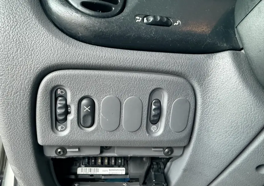 Gros plan sur les commandes grises du tableau de bord de la Renault Mégane, avec interrupteurs et boutons variés.