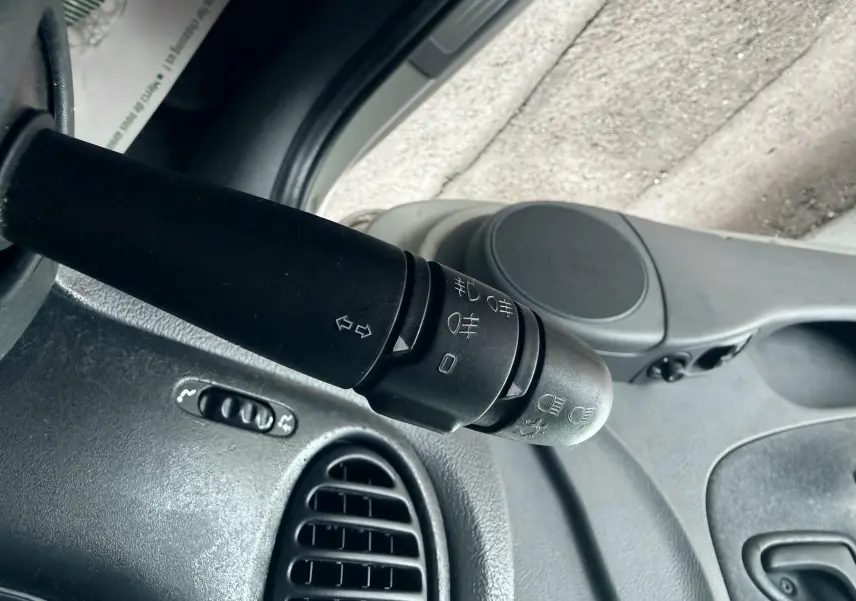 Gros plan sur la commande des phares et clignotants côté gauche du tableau de bord gris d’une Renault Mégane verte.