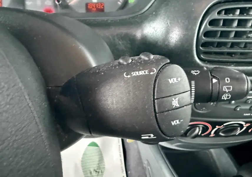 Gros plan sur la commande audio au volant d’une Renault Mégane verte, tableau de bord et aérateurs en arrière-plan.