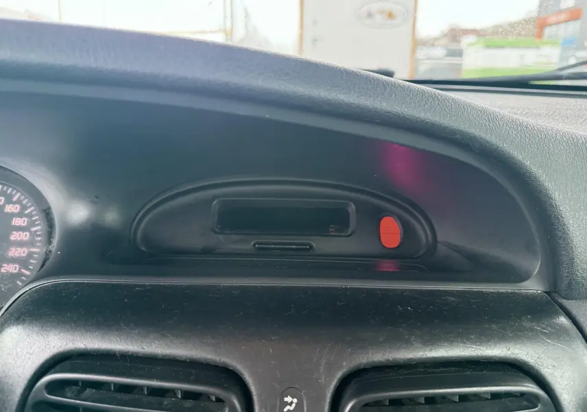 Gros plan sur le tableau de bord noir de la Renault Mégane 2000 avec affichage digital et bouton d'alerte rouge.