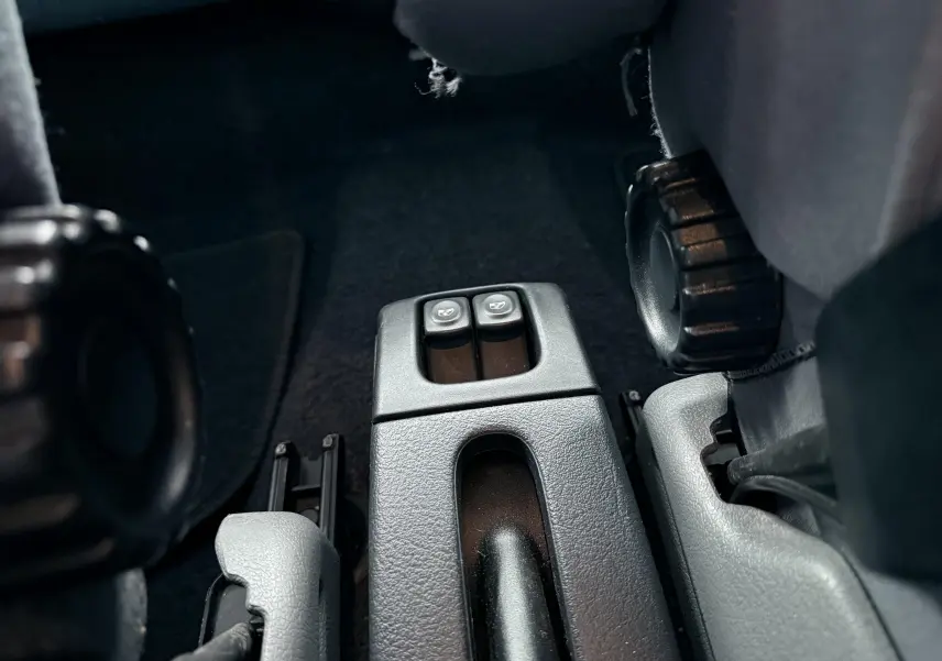 Gros plan sur les commandes de lève-vitres arrière entre les sièges avant d’une Renault Mégane verte de 2000.