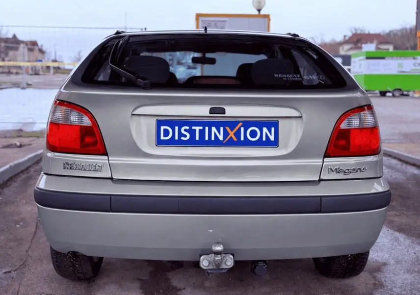 Vue arrière d'une Renault Mégane verte de 2000 avec attelage et plaque Distinxion visible.