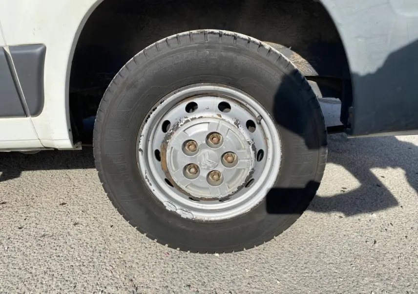 Gros plan sur la roue avant droite d'un Citroën Jumper blanc de 2013 avec jante acier et écrous rouillés.