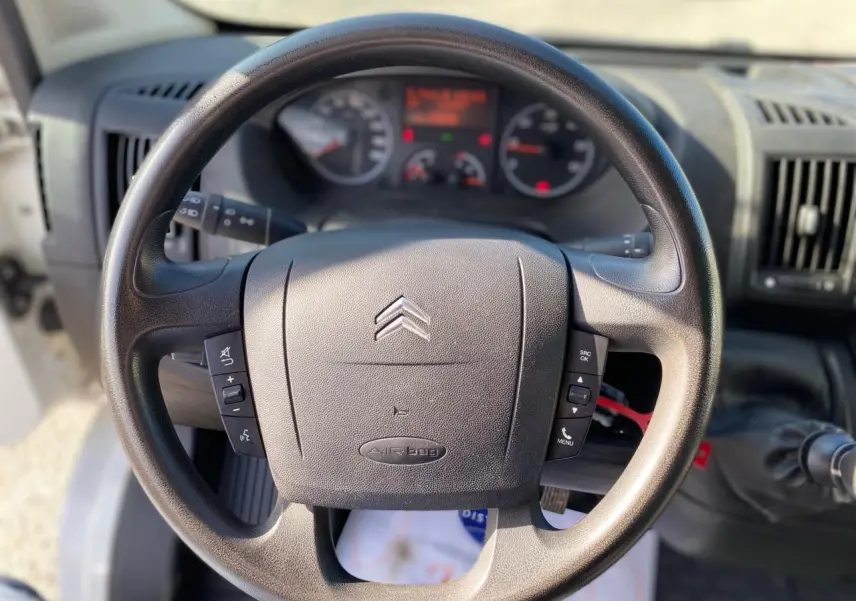 Volant noir de Citroën Jumper 2013 vu de face, avec commandes intégrées et tableau de bord flou en arrière-plan.