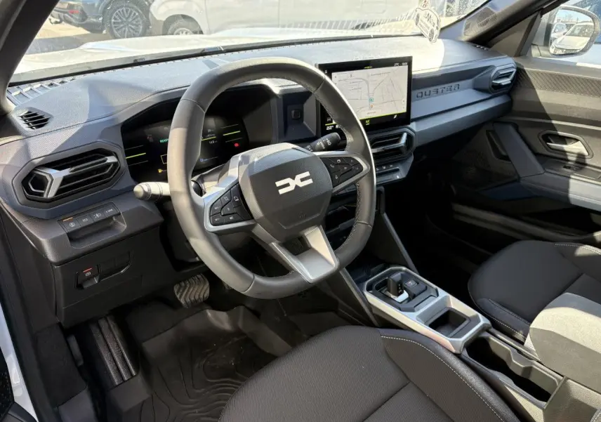Vue intérieure côté conducteur du Dacia Duster 2024 blanc métallisé, avec tableau de bord digital et écran tactile central.