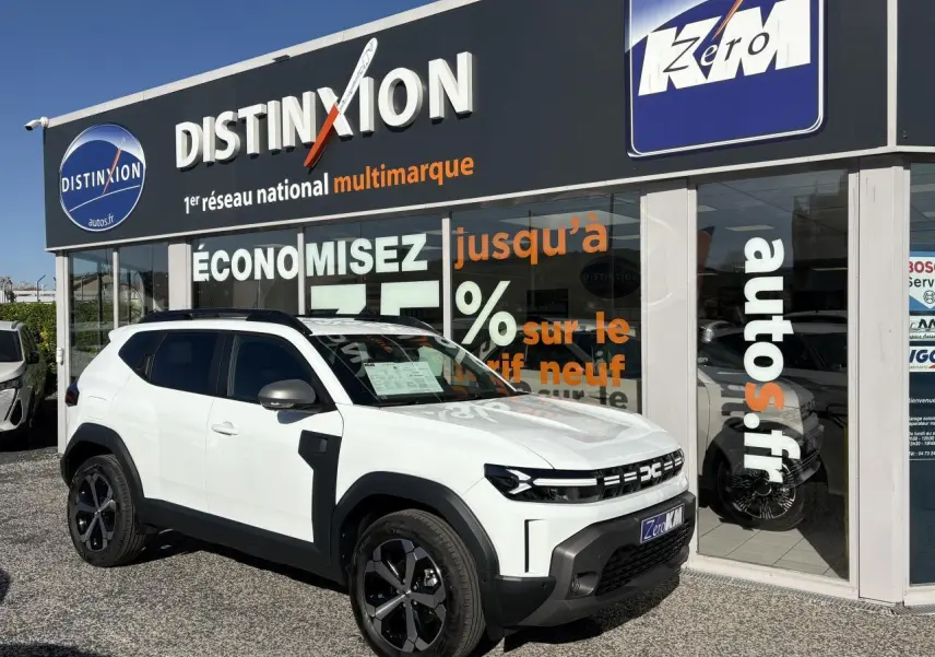 SUV Dacia Duster blanc métallisé vu de 3/4 avant droit, avec jantes alliage noires et barres de toit noires.