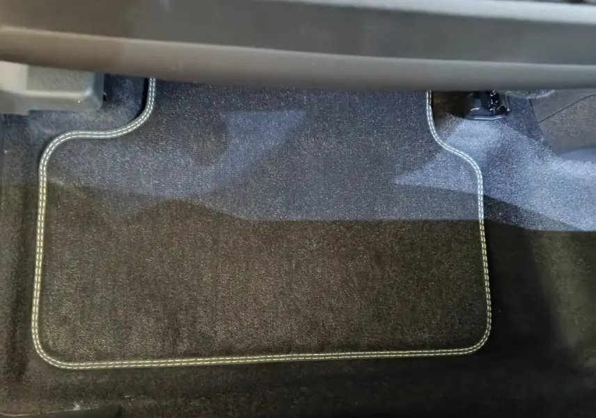 Tapis de sol noir avec surpiqûres blanches dans l'habitacle avant d'un Peugeot 3008 gris clair hybride 2025.