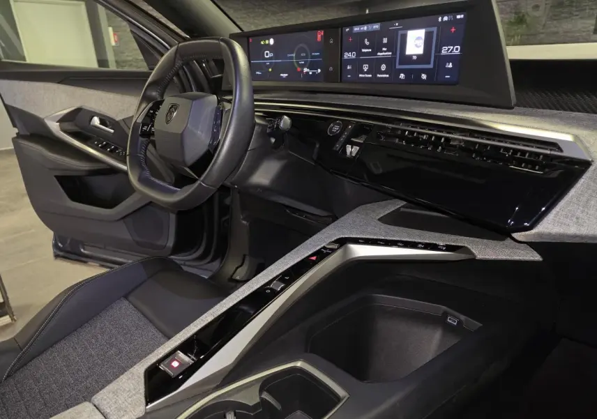 Vue intérieure côté conducteur du Peugeot 5008 gris 2025, mettant en valeur le tableau de bord numérique panoramique et la console centrale design.