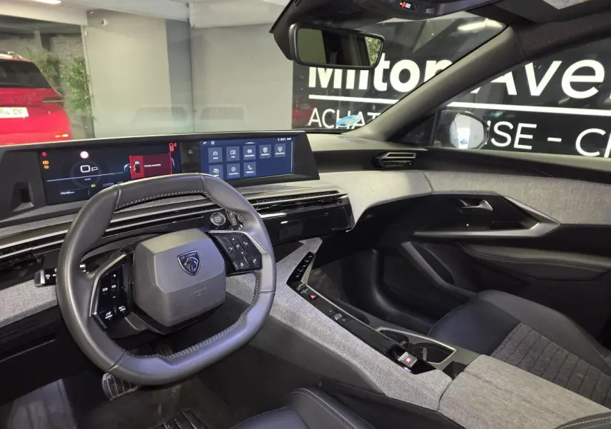 Vue intérieure côté conducteur du Peugeot 5008 gris 2025, avec tableau de bord numérique panoramique et volant compact cuir.
