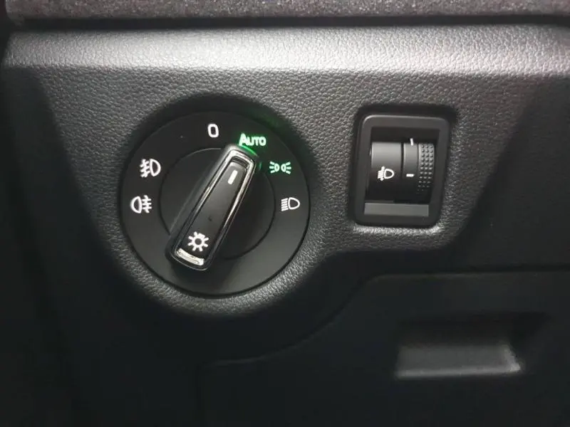 Gros plan sur la commande des phares avec réglage d'intensité, tableau de bord noir du Skoda Kamiq gris diamant.