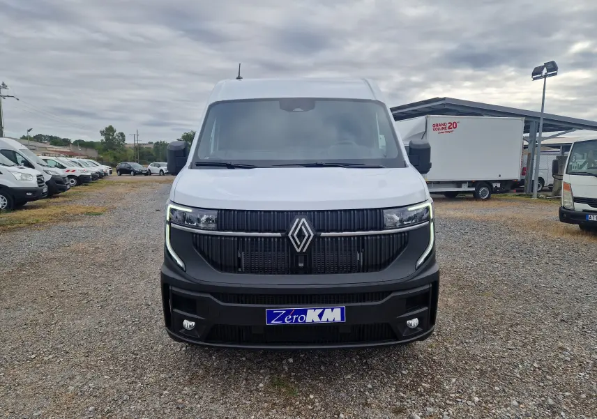 Vue frontale d’un Renault Master blanc 2026 avec calandre noire et feux LED en forme de C, sur parking extérieur.