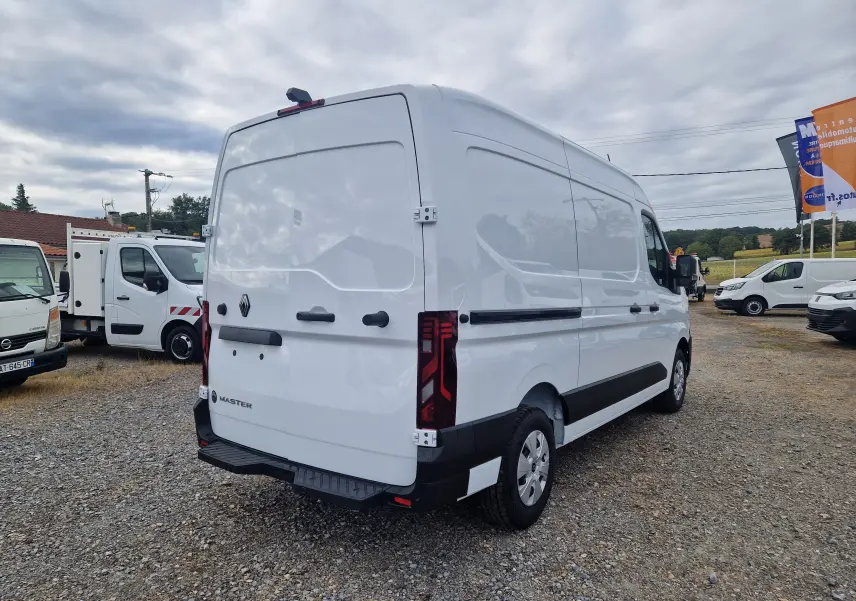 Vue 3/4 arrière droite d’un utilitaire Renault Master blanc, avec feux arrière LED et porte arrière fermée sur un sol gravillonné.