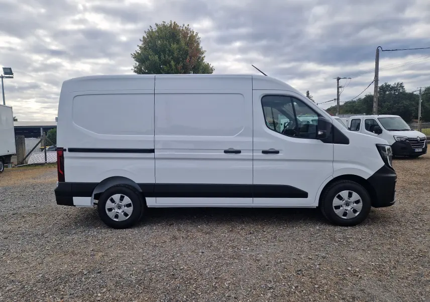Vue de profil côté droit d’un Renault Master blanc L2H2 avec bandeau noir et jantes acier, stationné sur un sol gravillonné.