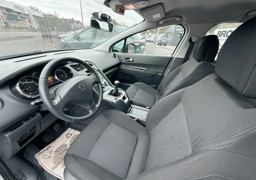 Intérieur avant du Peugeot 5008 2010 en tissu gris, vue côté conducteur avec volant et levier de vitesses manuel visibles.