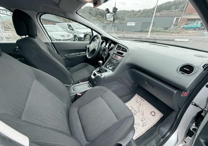 Intérieur du Peugeot 5008 gris 2010 vu côté passager, montrant les sièges tissu gris et la console centrale avec boîte manuelle.