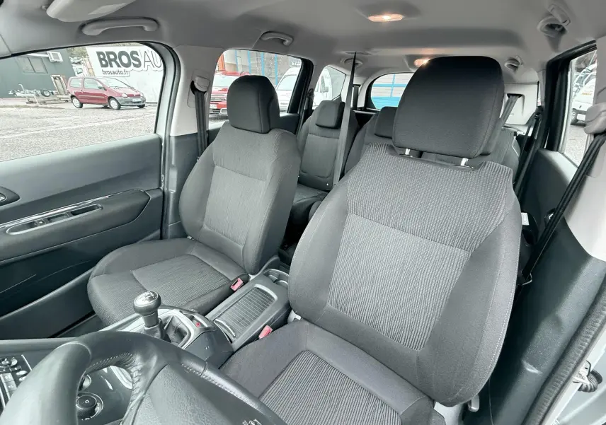 Vue intérieure du Peugeot 5008 gris, montrant les sièges avant et arrière en tissu gris avec volant cuir et levier de vitesse manuel.