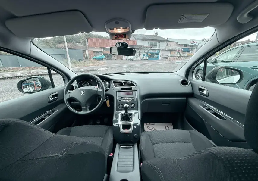 Vue intérieure avant du Peugeot 5008 gris de 2010, montrant le tableau de bord, volant et levier de vitesses manuel.